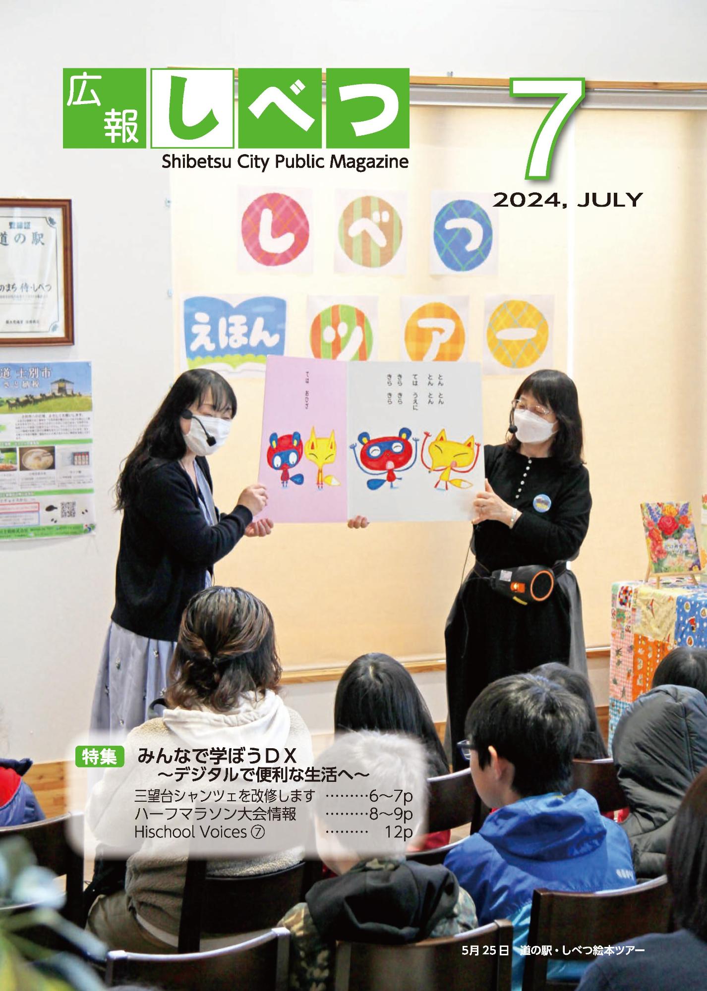 士別市広報7月号の表紙画像。女性2人が狐と狸が描かれている絵本を持って、子どもたちに朗読している様子。