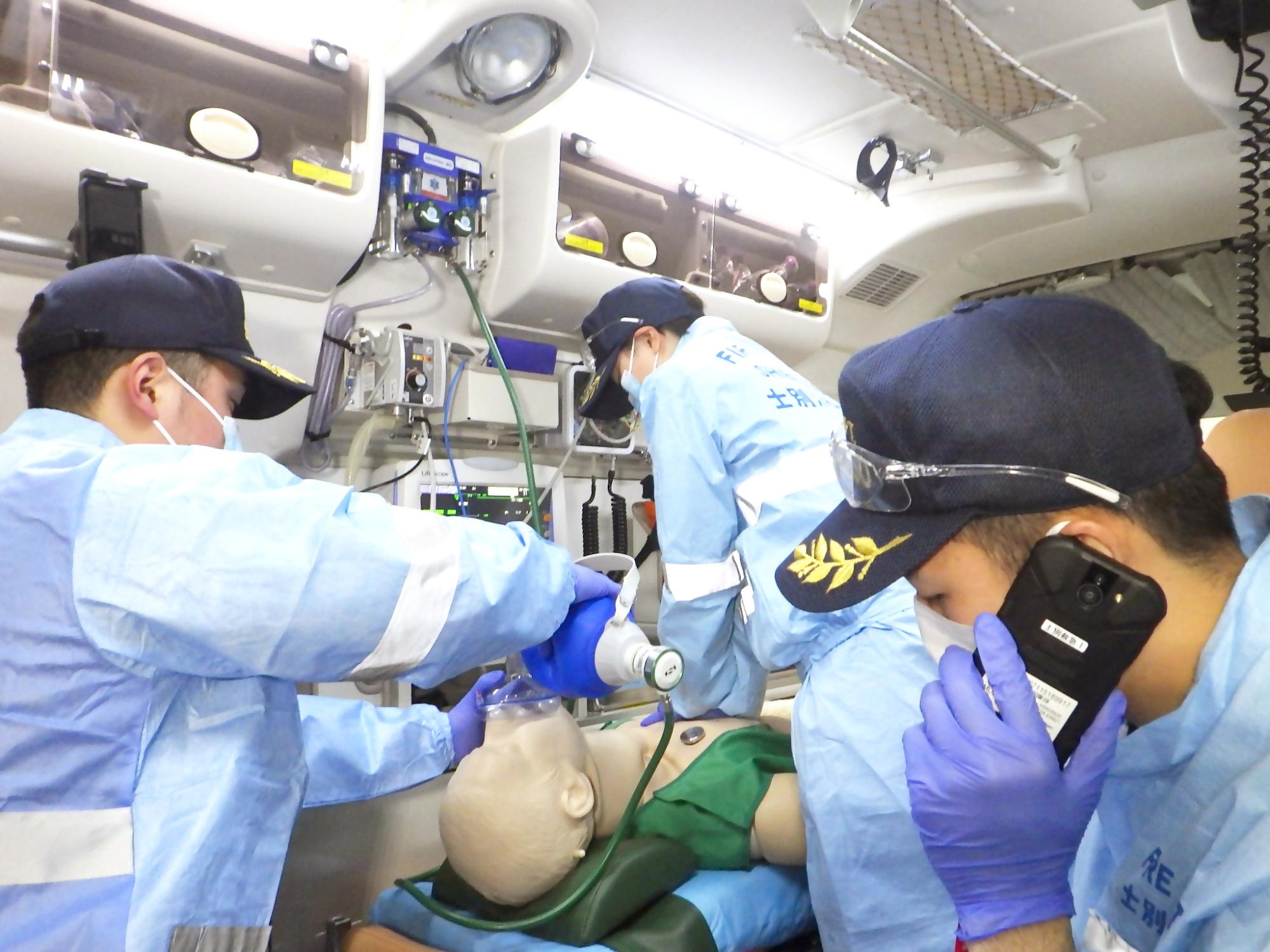 救急救命士の3人が本番を想定した訓練をしている。救急車の中で心肺蘇生や肺に空気を送っていたり、病院に症状を伝えるため電話をしている様子