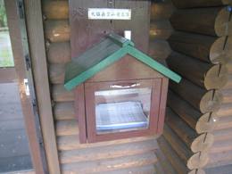 建物の外側に緑色の屋根で手前に倒せる取っ手がついている茶色の箱が設置された写真