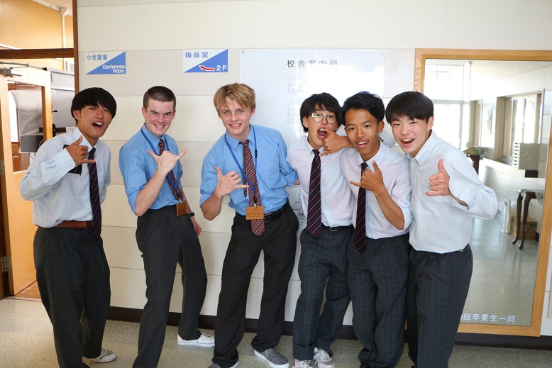 留学生の男子学生2名と男子高校生4名がろうかで楽しそうにポーズをとり記念撮影をしている写真