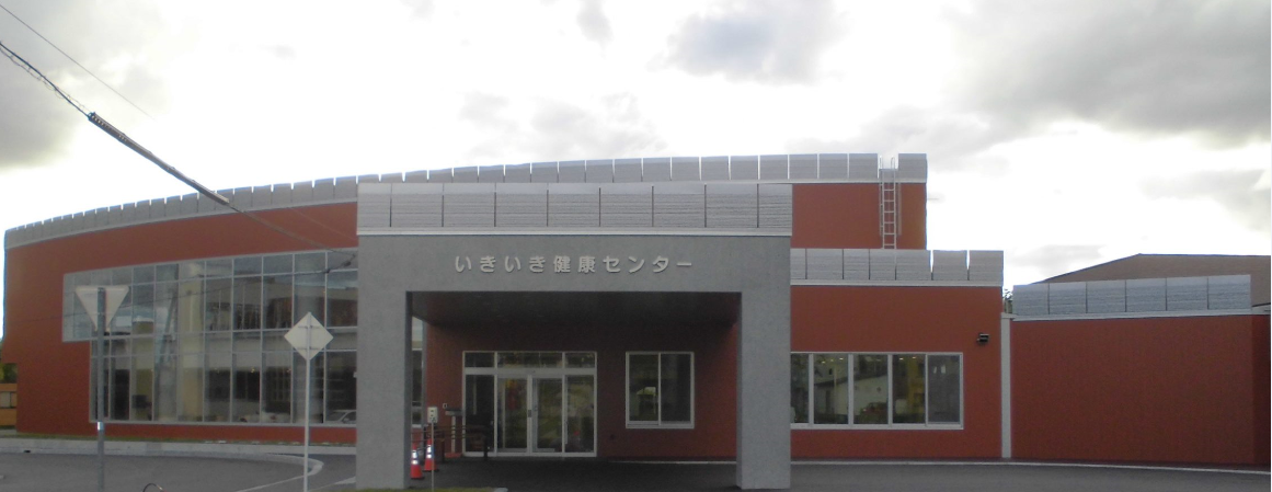 ガラス張りで壁が朱色とグレー色で施された、いきいき健康センター建物外観の写真