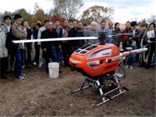 頂上のプロペラが回っている小型のヘリコプターの様な機械を周囲で見ている人達の写真
