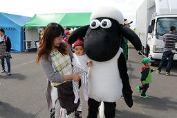 「ひつじのショーン」の着ぐるみの傍に赤ちゃんを抱っこしている女性が近寄って喜んでいる写真
