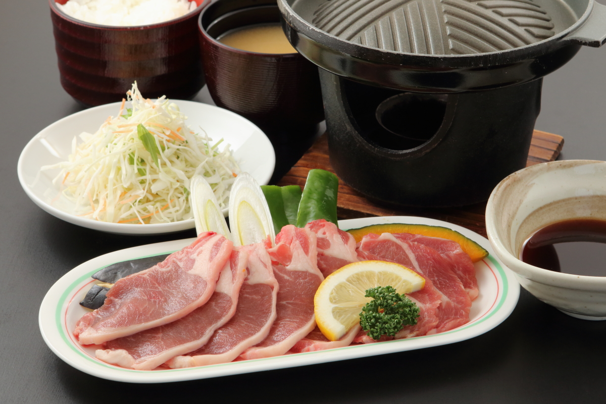 ジンギスカン用の鉄板鍋とごはん、味噌汁サラダとラム肉の定食の写真