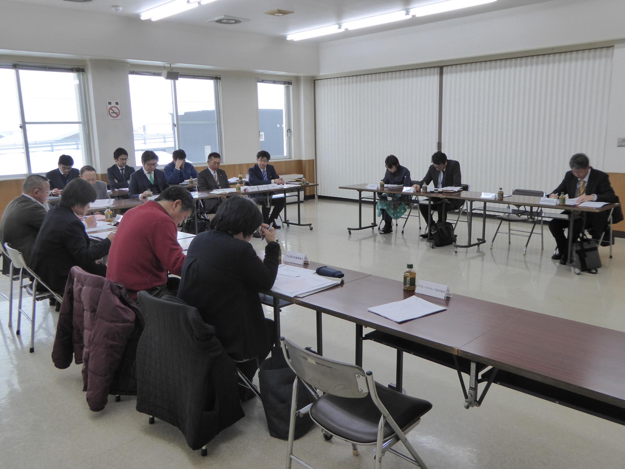 席について手元の資料を見ながら会議を行っている参加者の写真