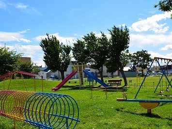 カラフルな滑り台、脇にブランコとうんてい、手前にシーソーとトンネル型のうんていがある公園の写真