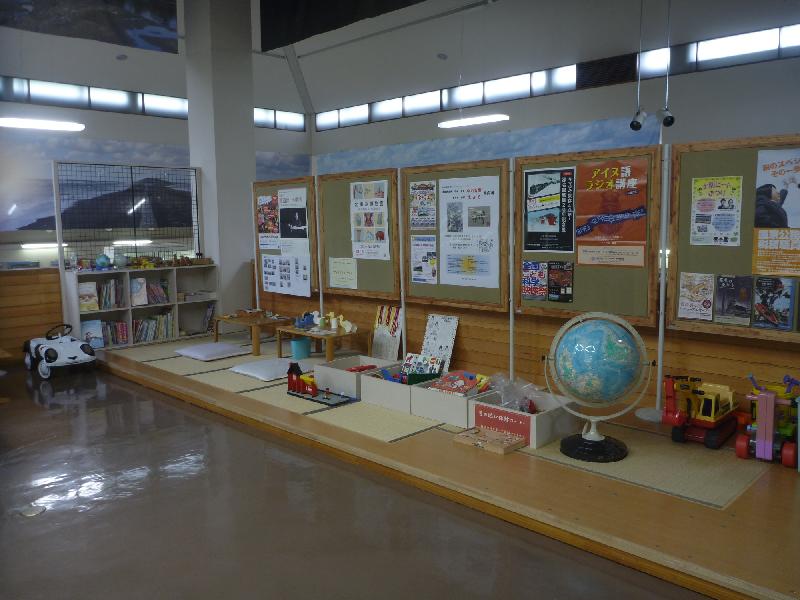 畳が敷かれた区画にたくさんのおもちゃや地球儀などが置かれ、掲示板にポスターなどが貼られている畳コーナーの写真