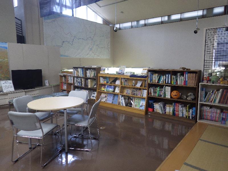 四人掛けの円卓の奥に本棚が並べられている図書資料コーナーの写真
