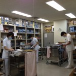 3名の白衣を着た方々が注射処方箋を見ながら薬品庫から薬剤を取り出している注射剤調剤業務の写真
