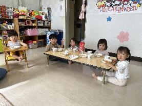 停車している黄色い通園バスの横で、保育士の前に帽子とカバンを持った園児5名が並んでいる写真