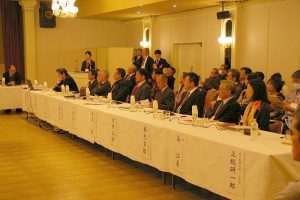 白いテーブルクロスが掛けられた席に座っている参加者の方々と、その方たちの後ろに座っている多くの参加者達の写真