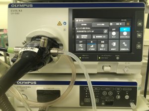 左側にチューブなどが取り付けられ、右側に操作パネルが見えるオリンパス製次世代内視鏡システム(EVIS X1)の写真