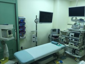 中央にベッド、ベッドの周りに沢山の機械やモニターが置かれている検査室のような室内の写真