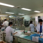 様々な薬が棚に保管されており、薬剤師の方々が処方箋を見ながら薬剤を調合している様子の写真