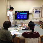 「糖尿病の分類と治療法」がモニターに映し出され、白衣を着た男性が女性2名に説明している糖尿病教室の写真