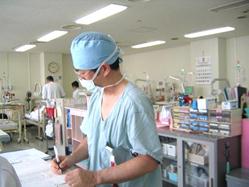 帽子とマスクを身に着けた担当医師がカルテに記録をしている様子の写真