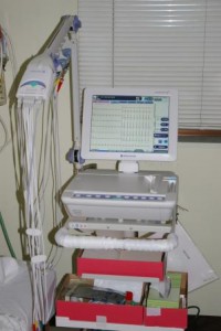 中型の画面に波形が表示され、左側に沢山のコードがぶら下がっている誘導心電図の機器の写真