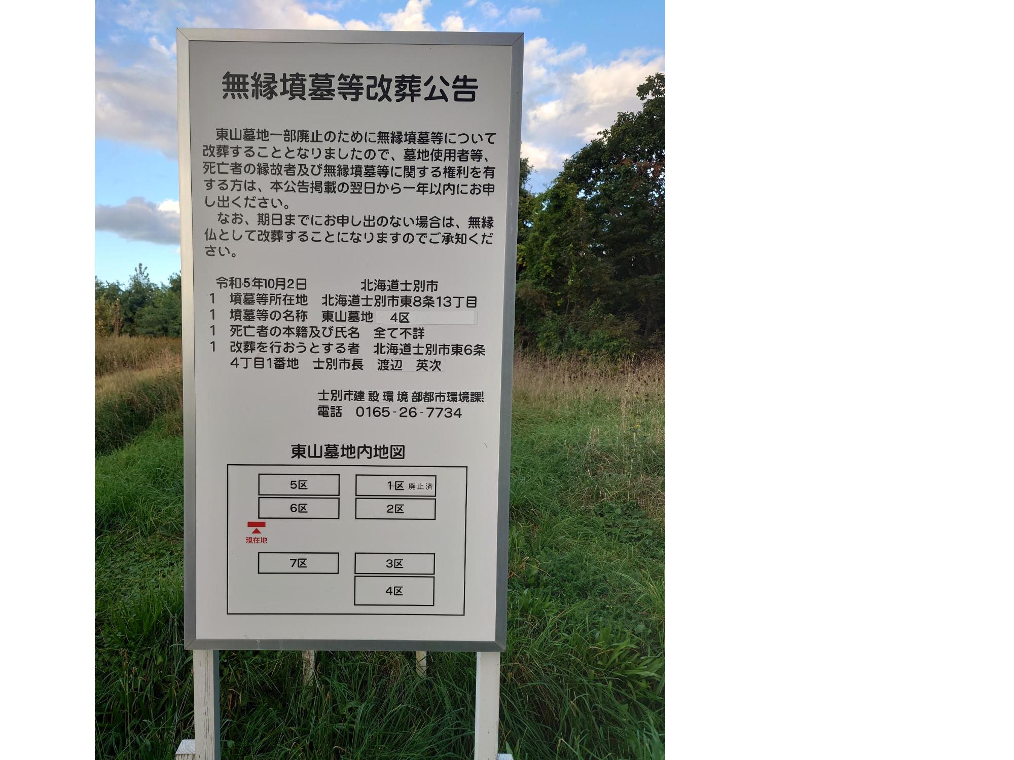 緑が広がる草原の北側出入口に設置された無縁墳墓等改葬広告の看板の写真