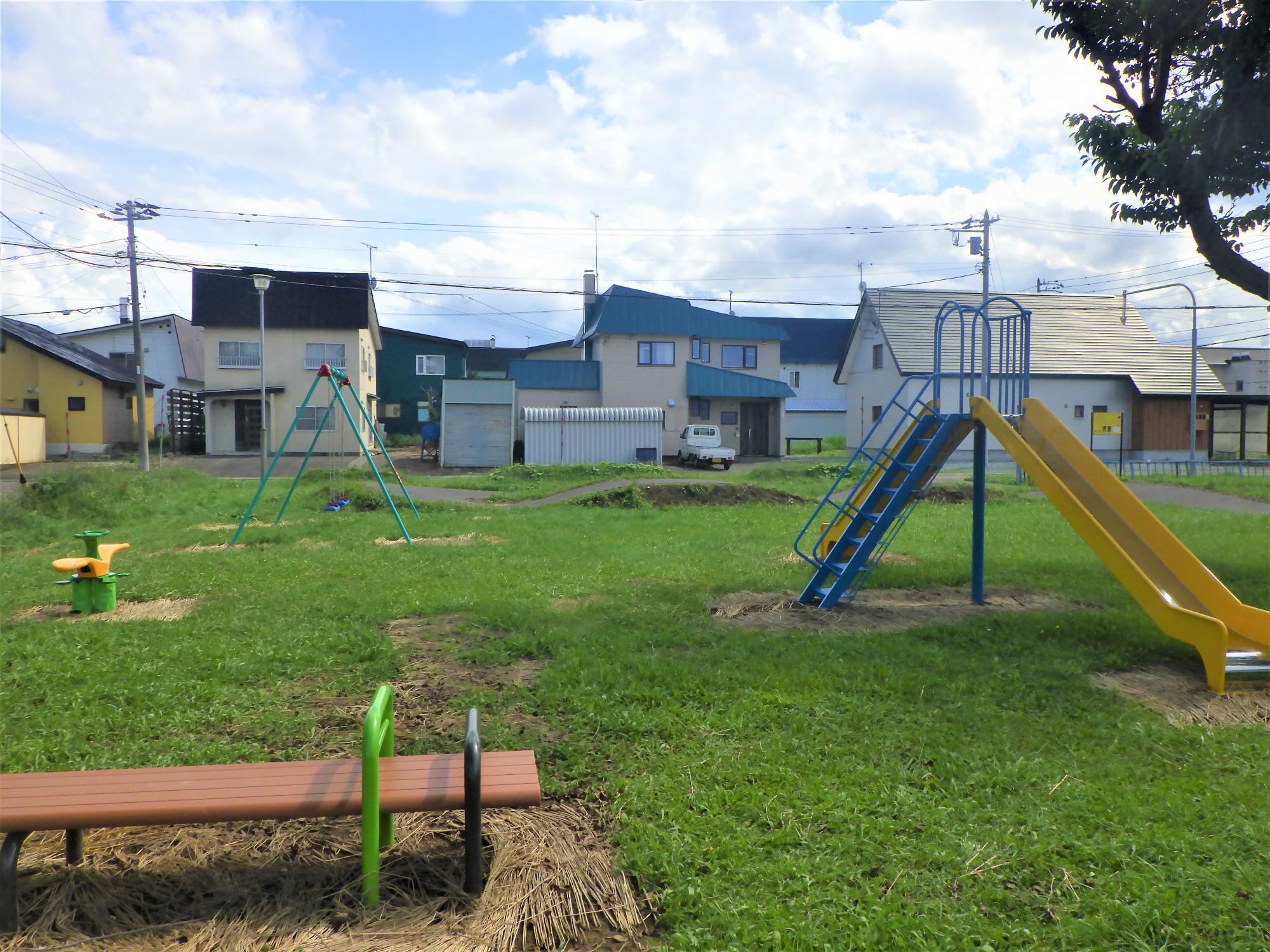 2方向滑り台やブランコなどが設置されている公園の写真