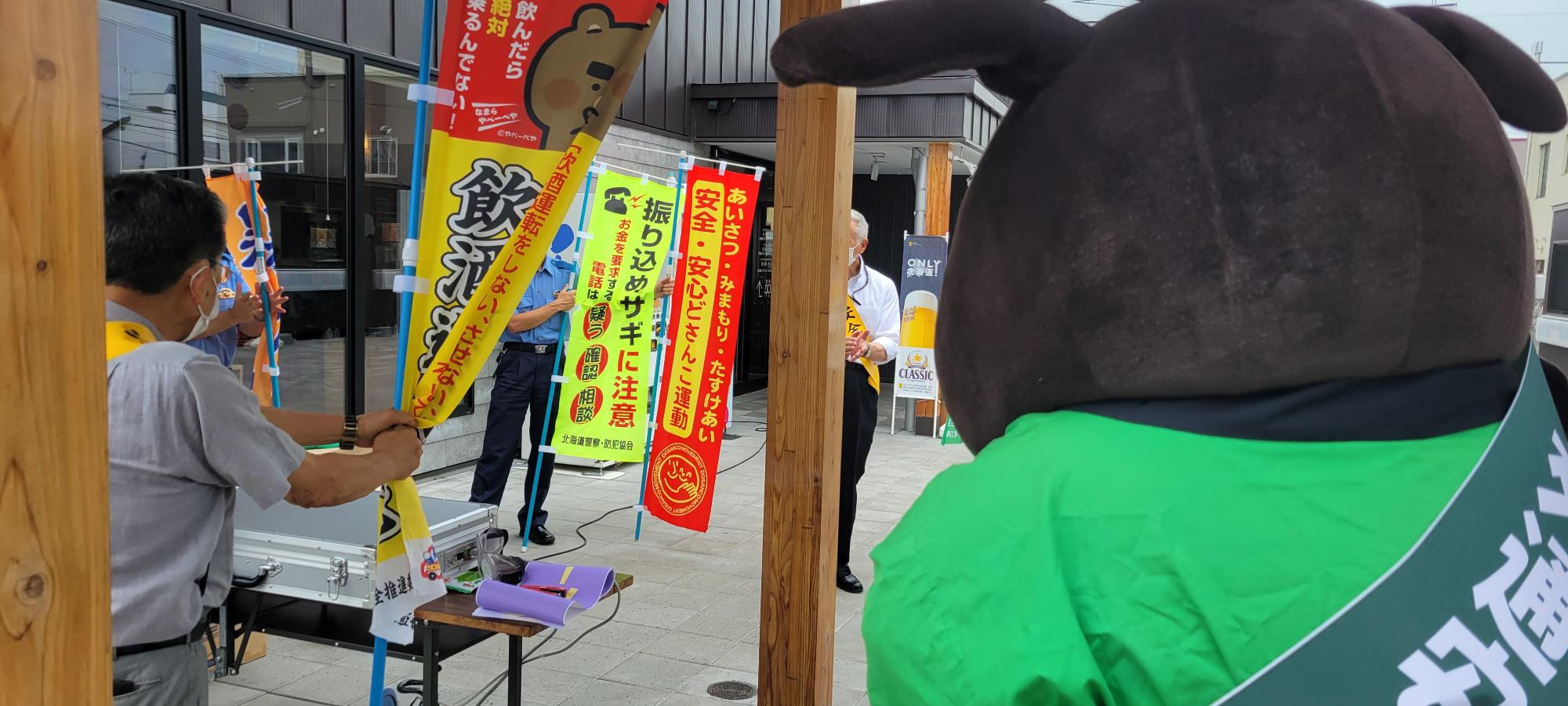 道の駅の建物入口の左側でのぼり旗を持って飲酒運転根絶の該当啓発活動を行っている安全協会の方達の写真