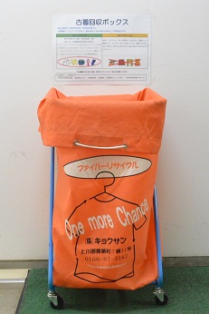 壁に古着の回収基準のチラシが貼られている手前に設置されたオレンジ色の回収ボックスの写真
