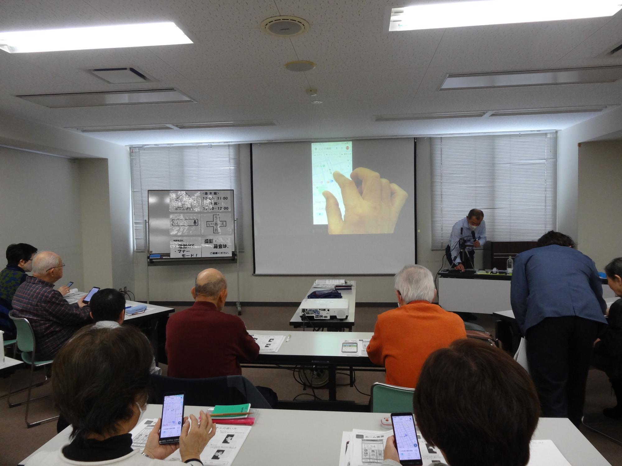 令和7年12月5日に行われたスマホ教室の様子。受講者の方がアシスタントの方に教えてもらいながらスマホの操作を実践している。