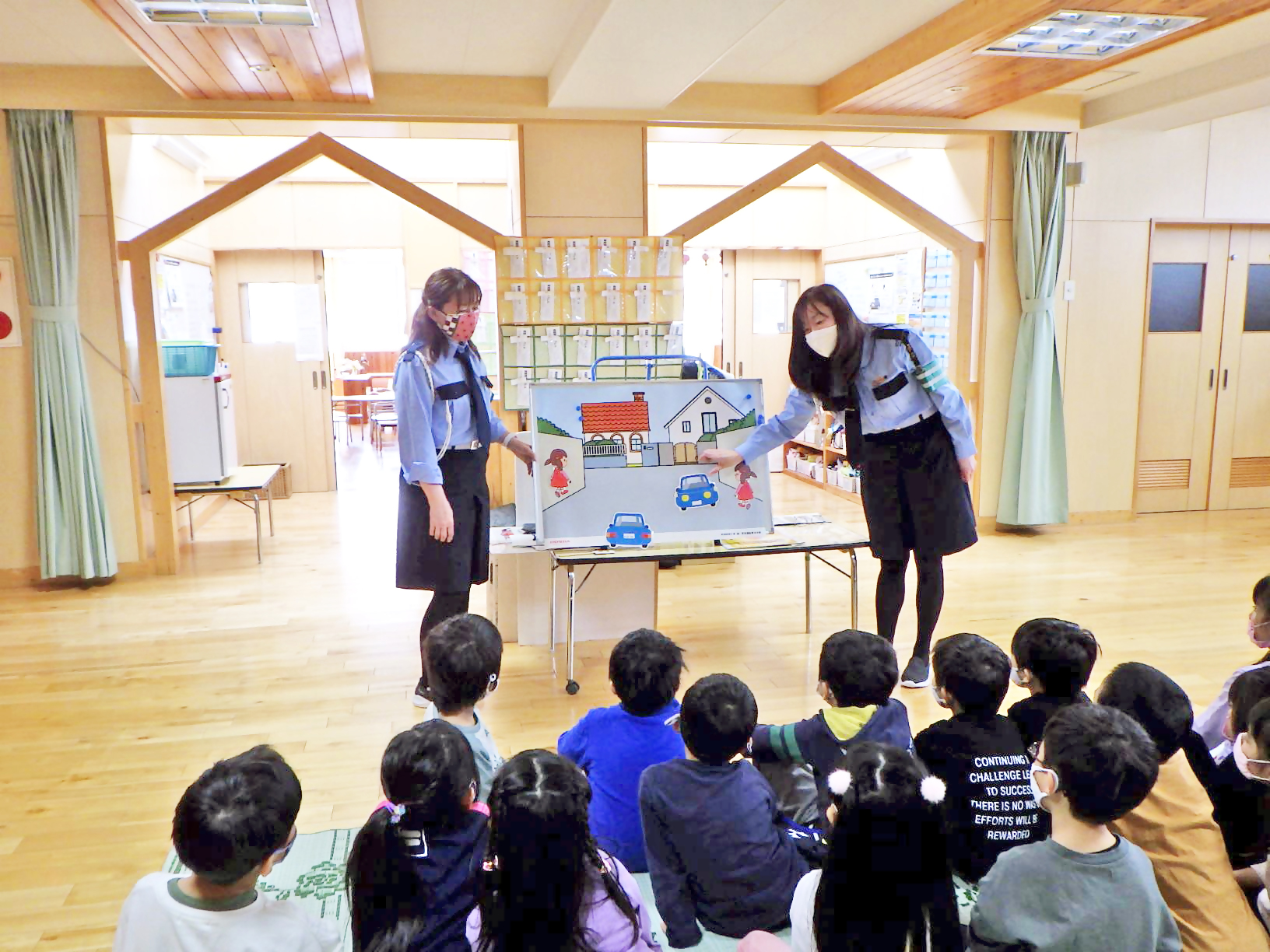 幼児施設で、子どもたちに紙芝居を使って交通安全について教えている「まもってあげ隊」隊員の写真。