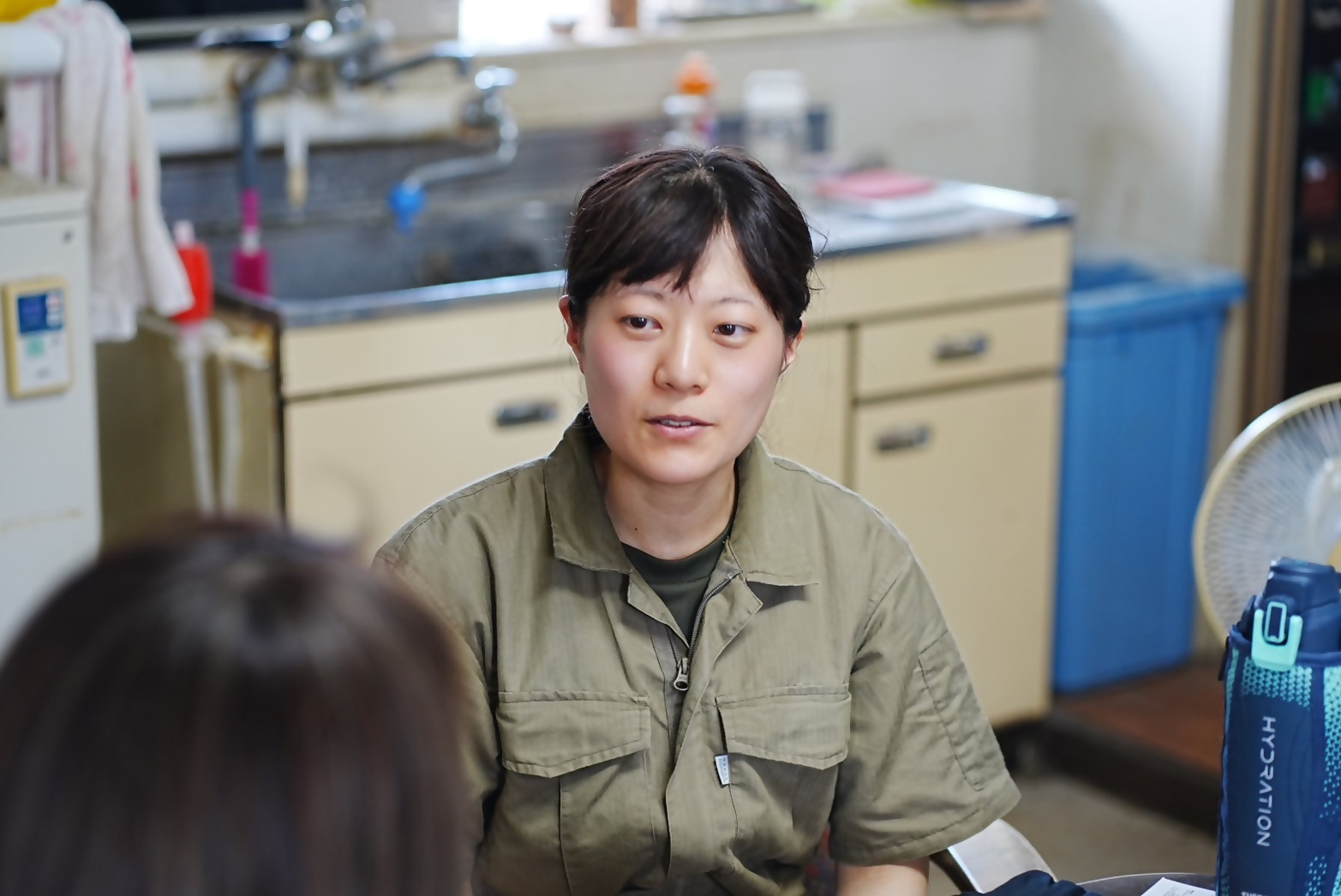 作業着を着ている女性が部屋の中で座っている様子