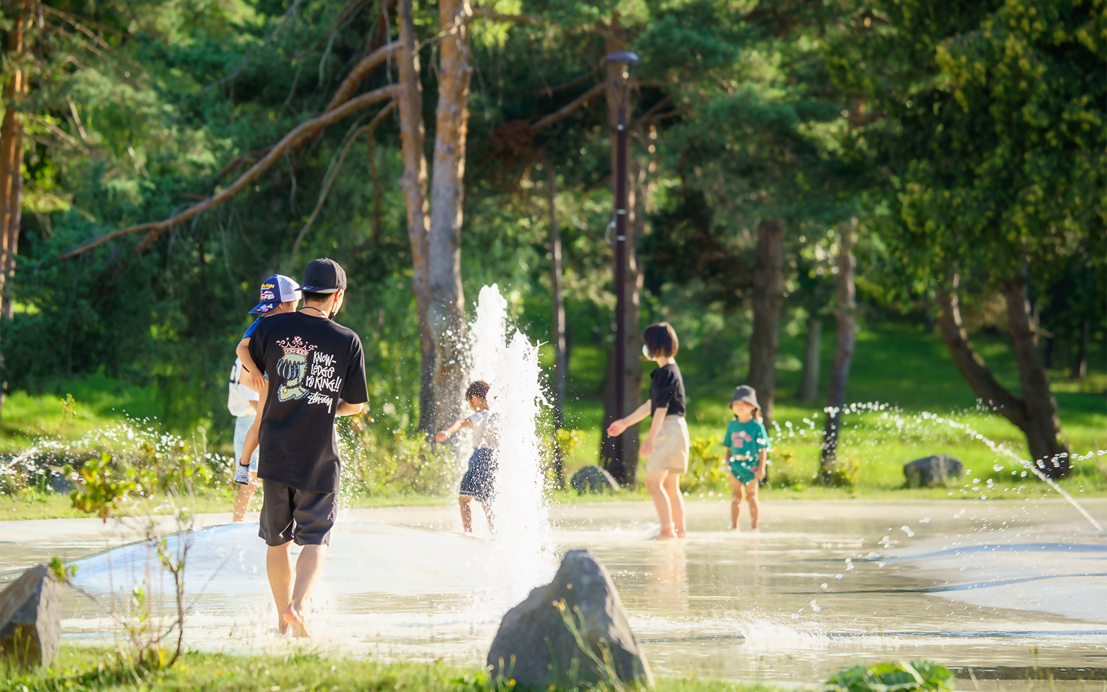 公園で大人と子どもが噴水の水で遊んでいる様子