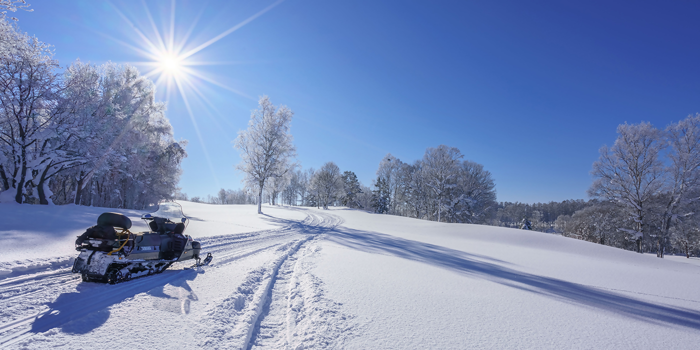 晴天のなか雪原にスノーモビルが置いてある写真