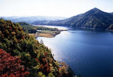 所々紅葉が色づく山々に囲まれた大きな湖の写真