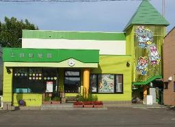 緑色の屋根に黄緑色の外壁、らせん階段の柵に象とウサギと熊の絵が描かれた士別幼稚園の建物の外観写真