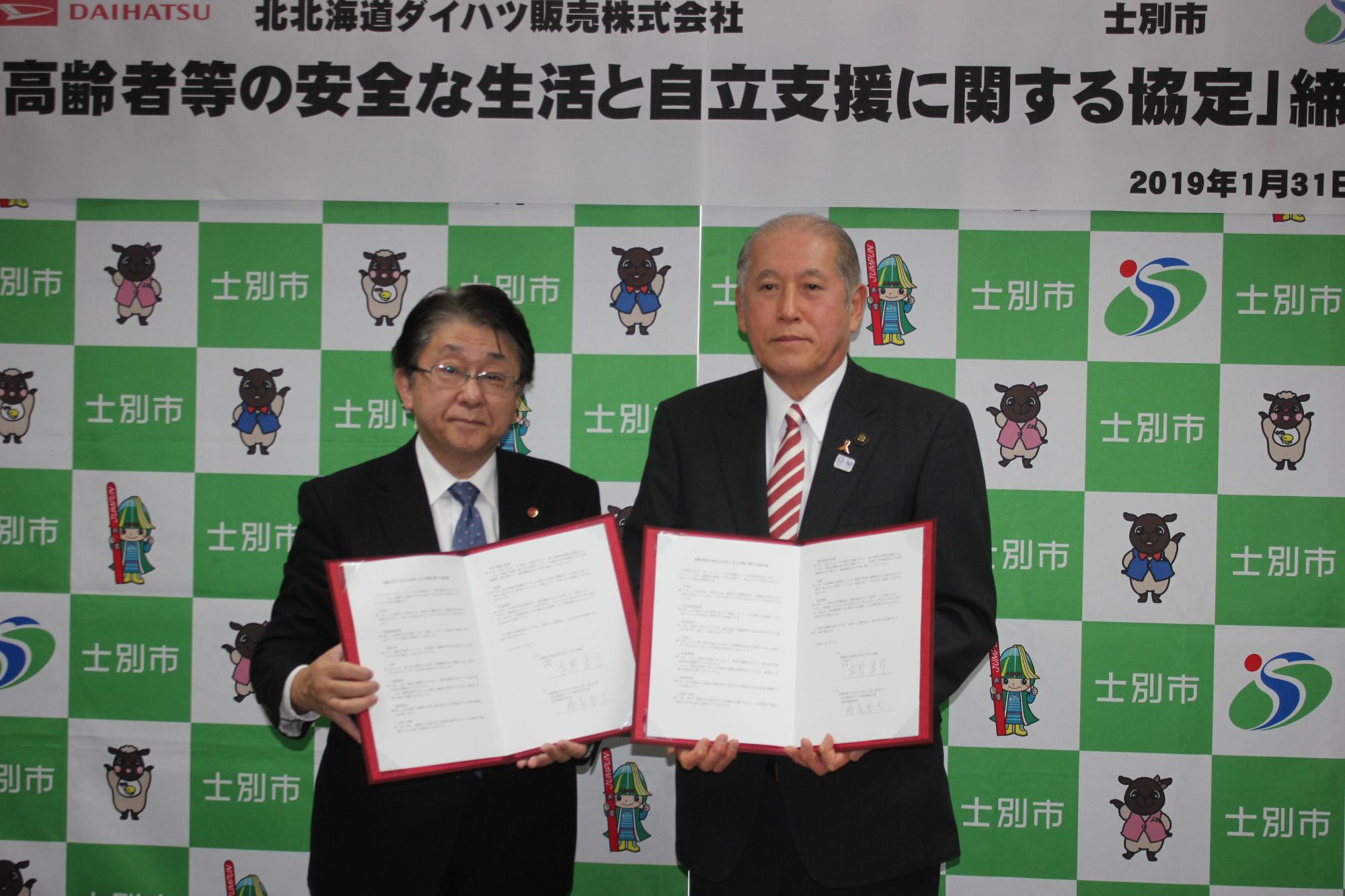 藤冨社長と市長が締結書を両手で持ちながら、北北海道ダイハツ販売株式会社との協定締結での記念撮影をしている写真