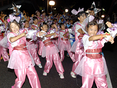 頭に大きなリボンを付け、全身ピンク色の衣装を着た参加者達が踊っている、いいじゃん祭りの写真
