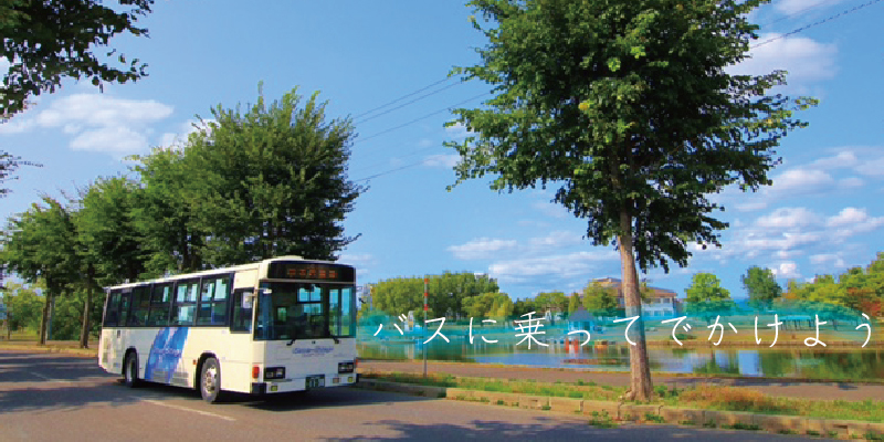 道路を走るバスの横に木々が並んでいる風景に「バスに乗ってでかけよう」と書かれた写真