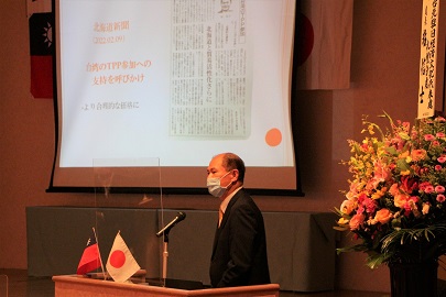 日本と台湾の小さな国旗の旗が飾られた壇上で1人の男性が講演を行っている写真