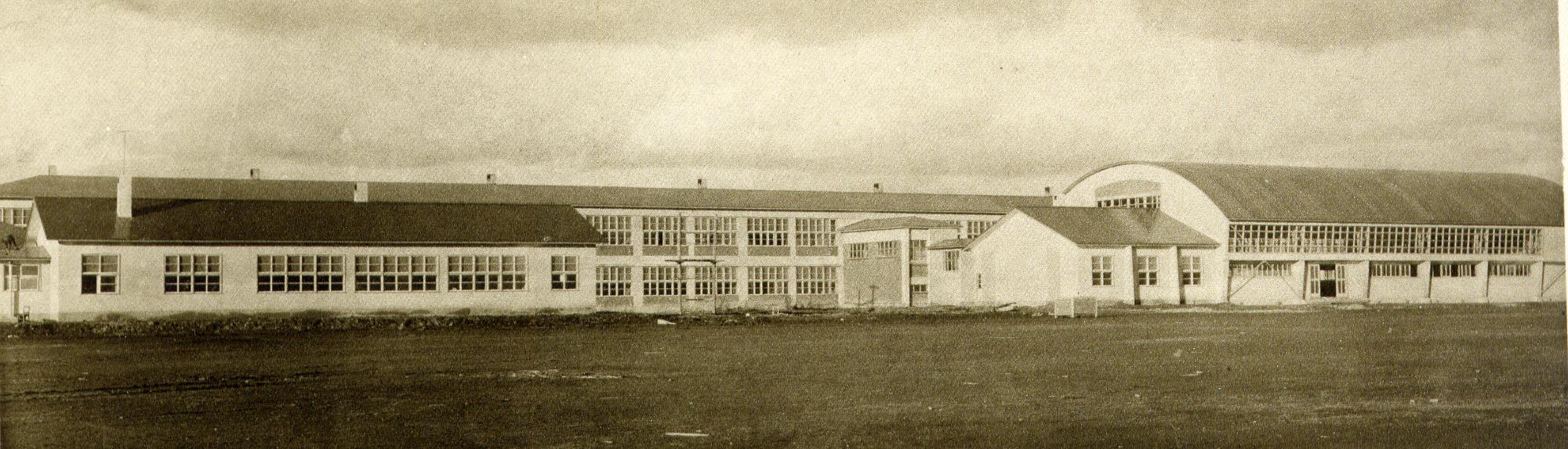 左側と奥に横長の校舎、右側に体育館が建てられた小学校を校庭から撮影した白黒写真