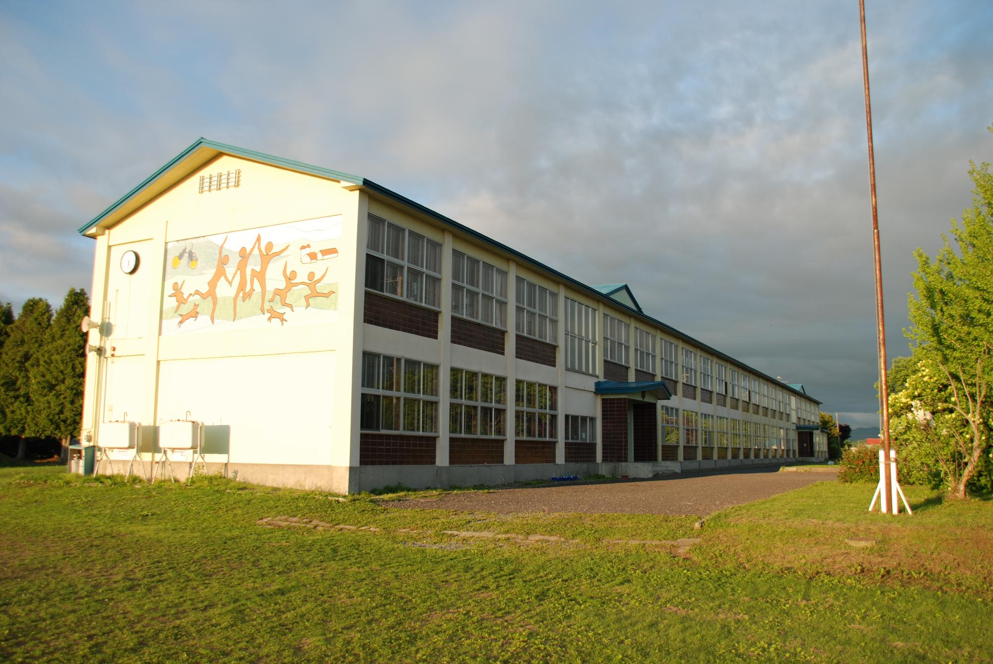 校舎横の壁に人の形をした壁画が描かれている2階建ての上士別小学校の校舎の写真
