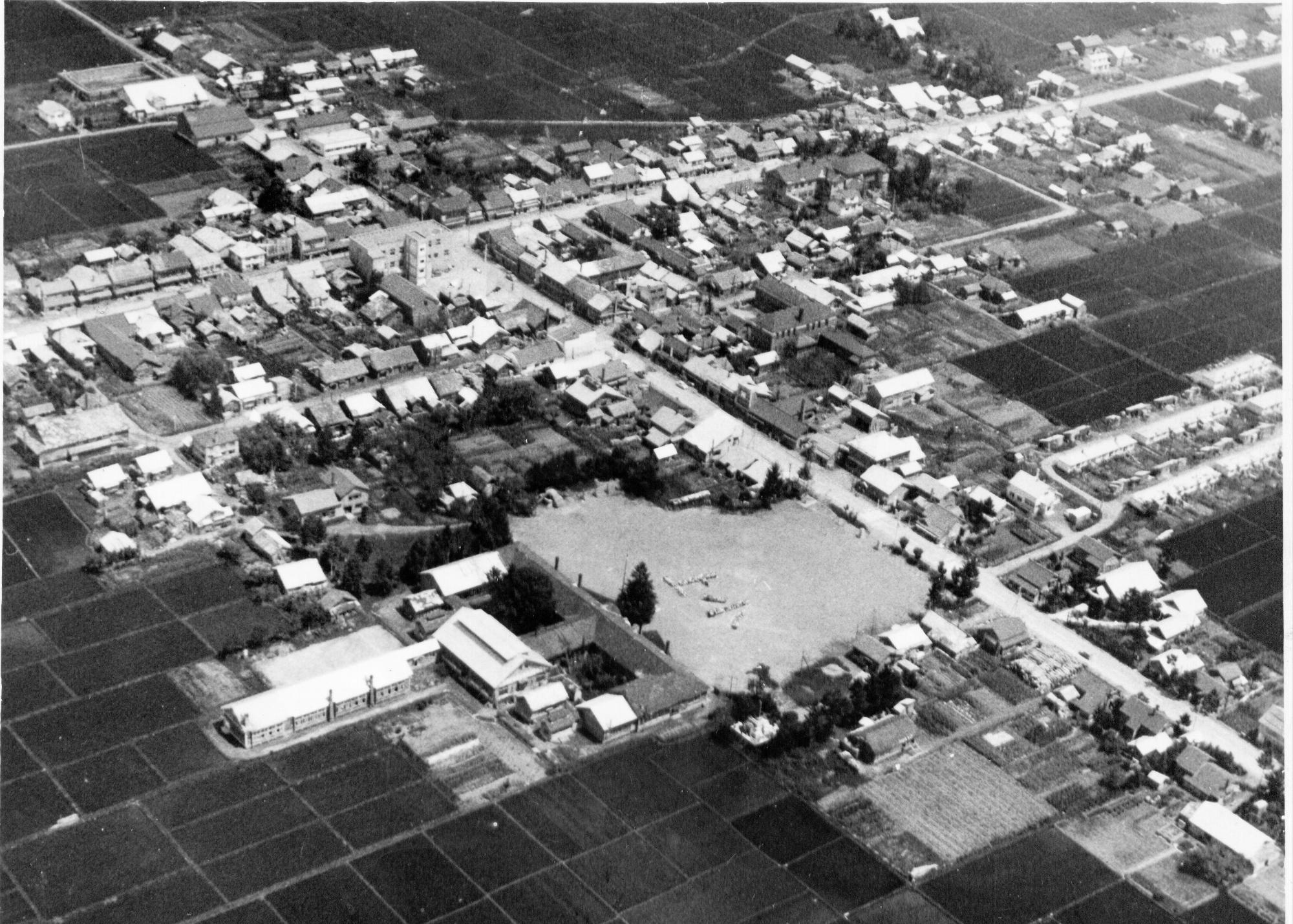 周囲に民家が建っている中央の校庭に「上小」と人文字で書かれた昭和30年頃の上士別小学校の航空写真