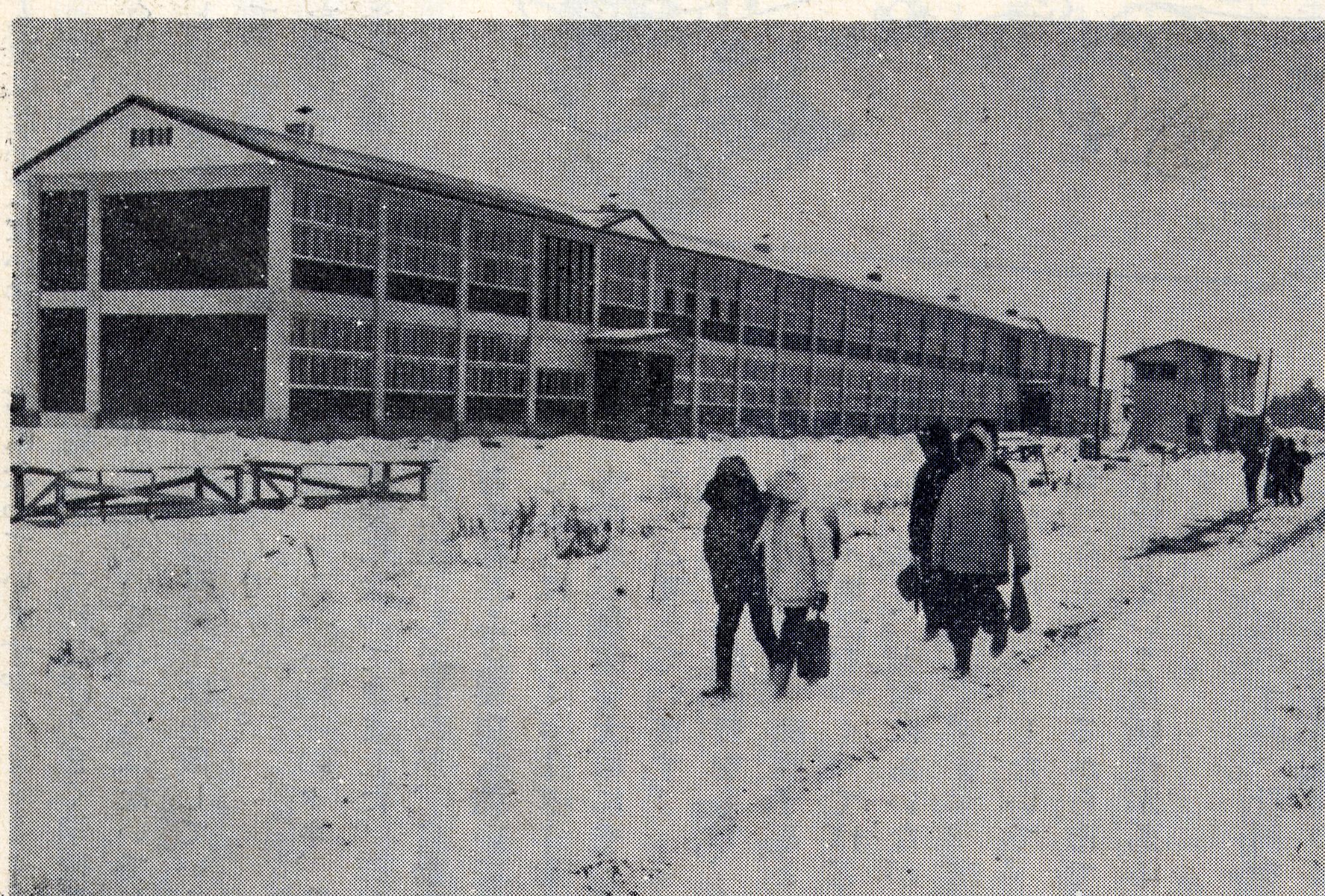 雪が積もった校庭を児童が歩いて登校している奥に建つ2階建ての上士別小学校の校舎の白黒写真