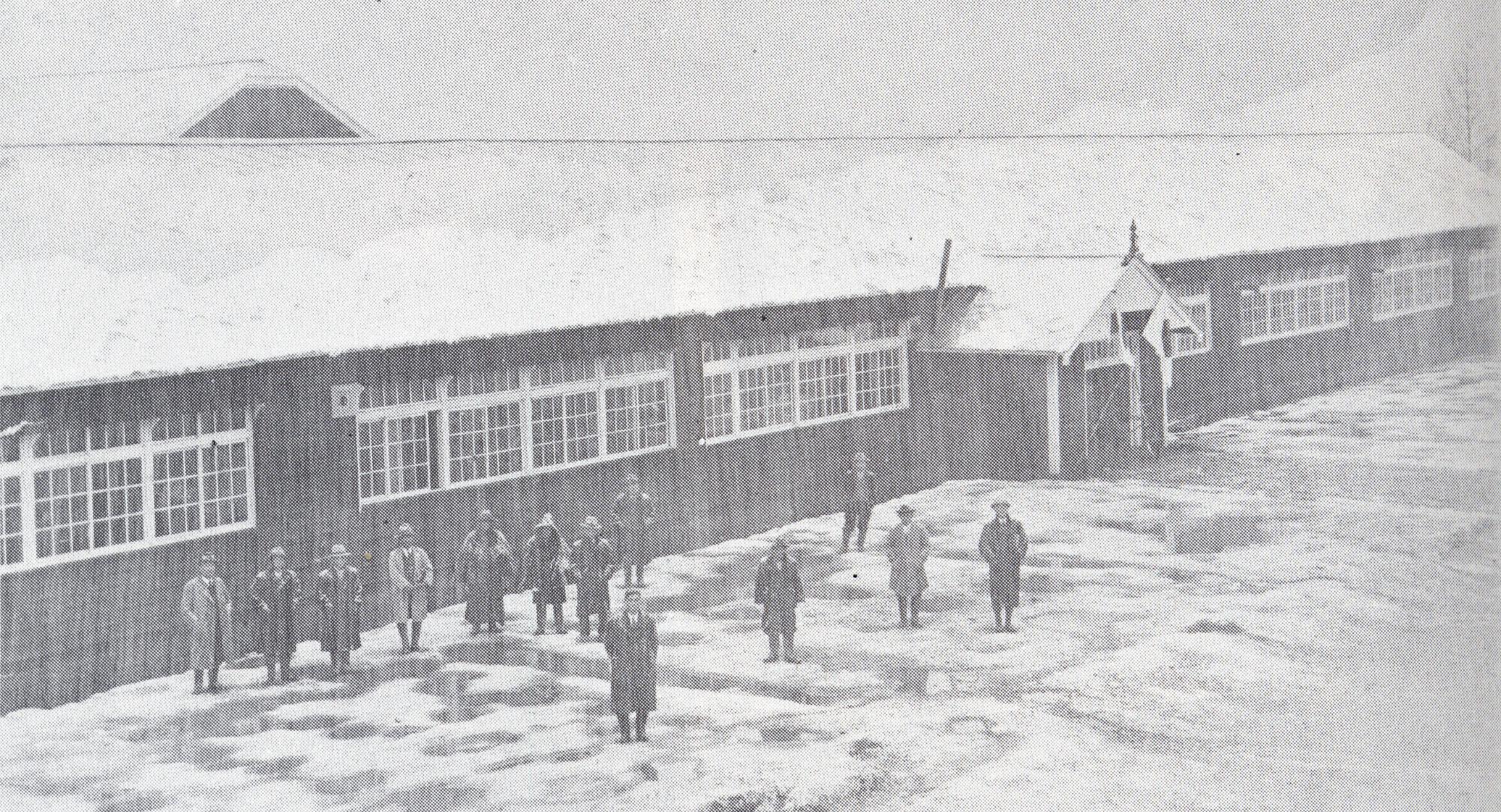 雪が積もった校舎の前に数名の男性が立ち上空を見上げている昭和10年頃の温根別小学校の校舎の白黒写真