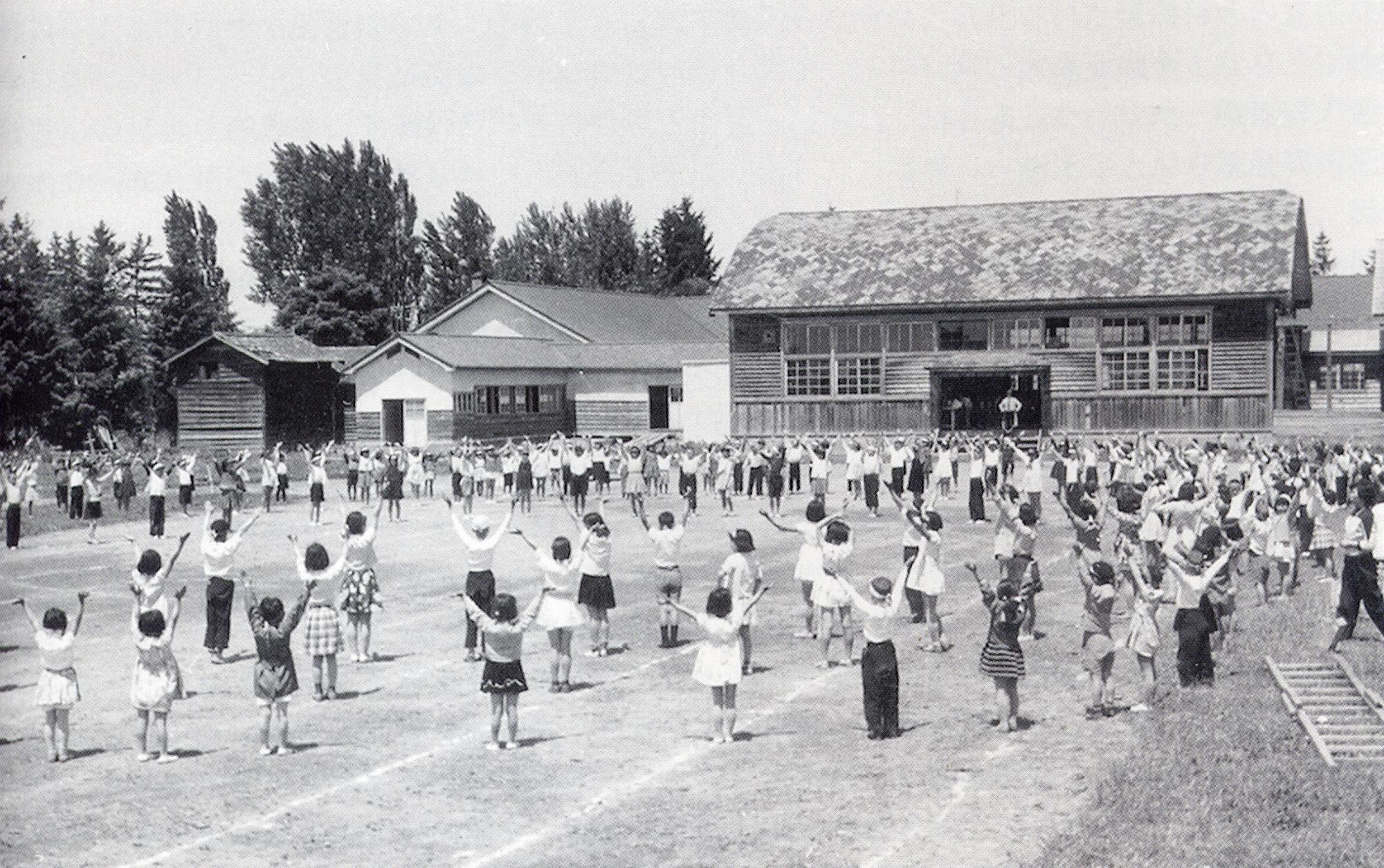 大勢の児童が両手を上に広げて体操を行っている校庭の奥に建つ昭和前半頃の武徳小学校校舎の白黒写真