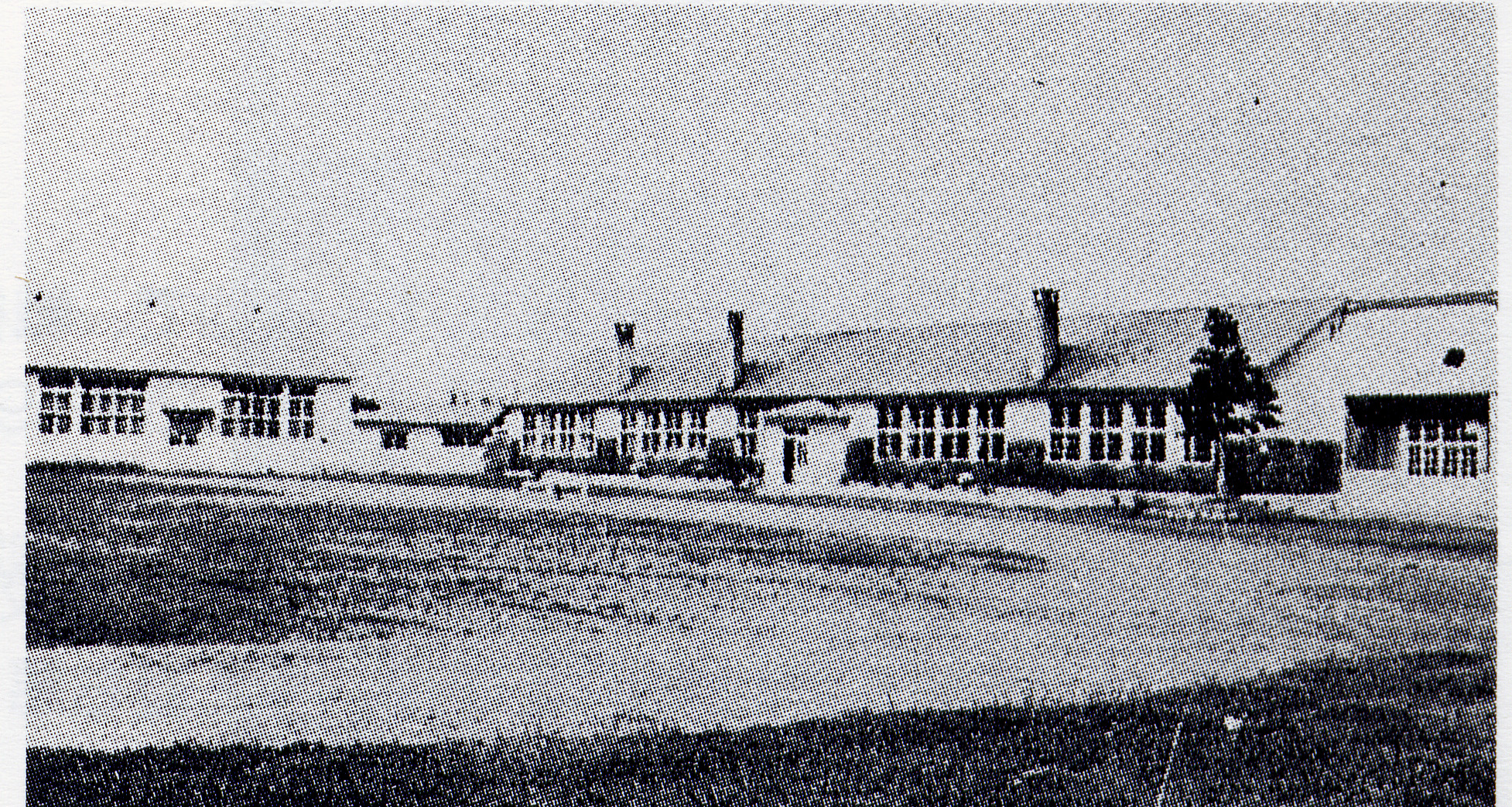 L字型で3本の煙突が設置された旧成美小学校校舎を校庭から撮影した白黒写真