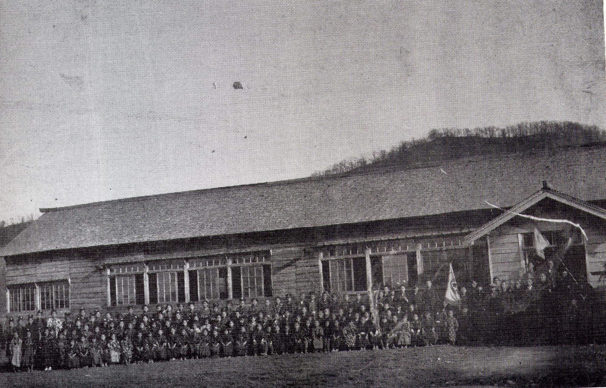 校舎の入り口から左側に大勢の児童が並んでいる大正時代の旧白山小学校校舎の白黒写真