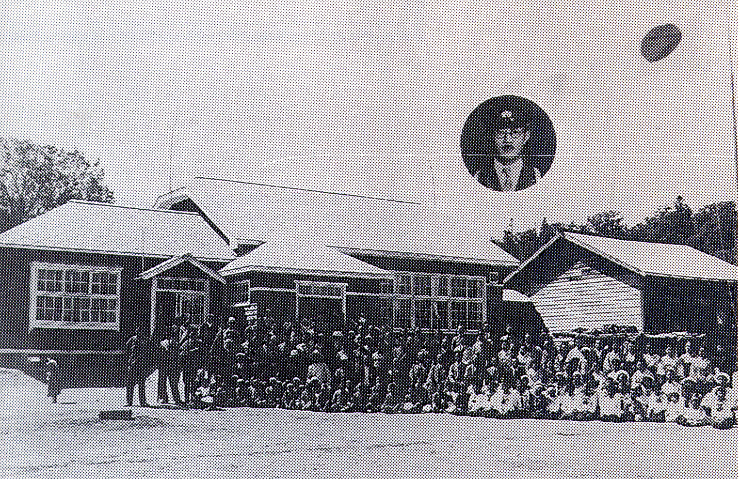 校舎の入り口の前で大勢の人達が並んでいる昭和10年代頃の旧北温小学校校舎の白黒写真