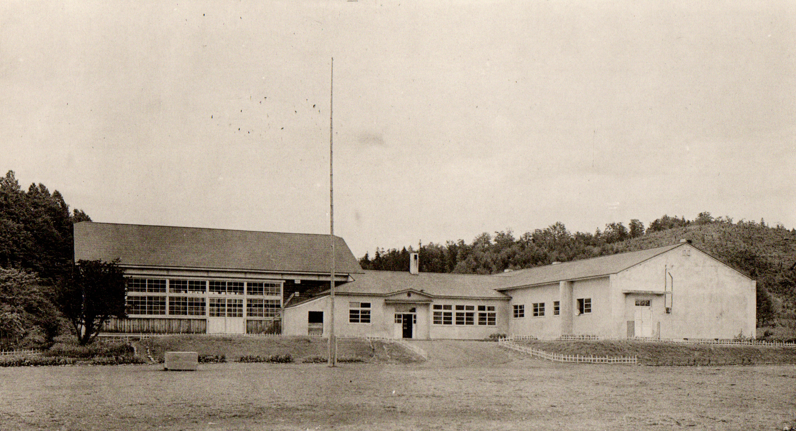 小高い丘の麓にL字型に建てられた旧壬子小学校校舎を校庭から撮影した白黒写真