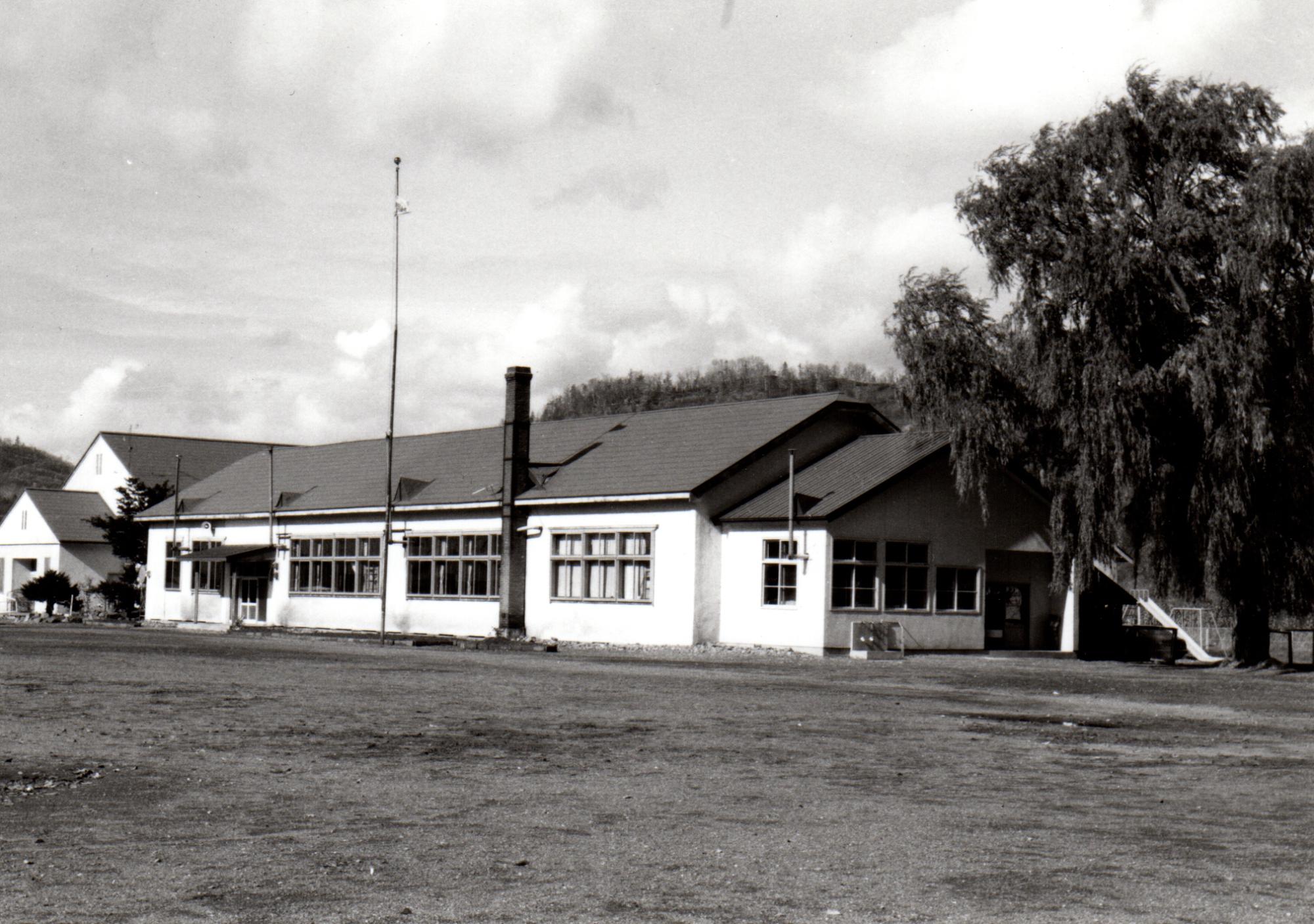 大きな木が立っている左側に建つ煙突が設置された旧登和里小学校校舎の白黒写真