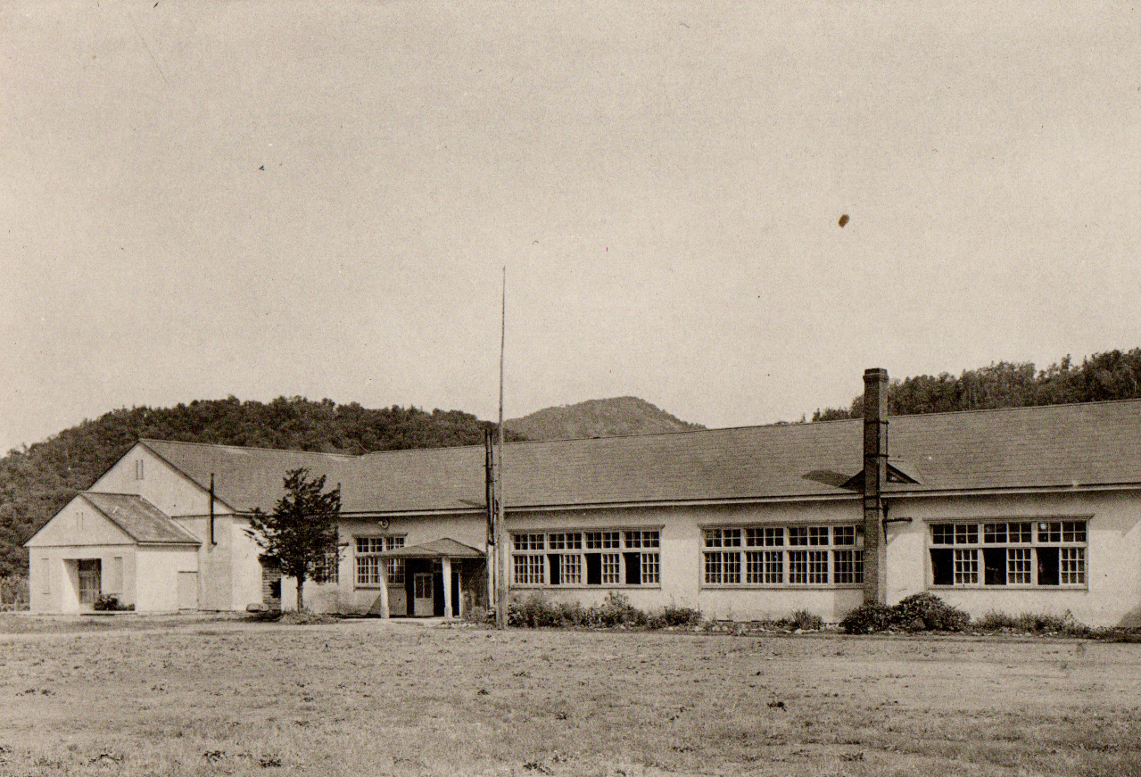 小山の麓に建てられた横長の昭和37年頃の旧登和里小学校校舎の白黒写真