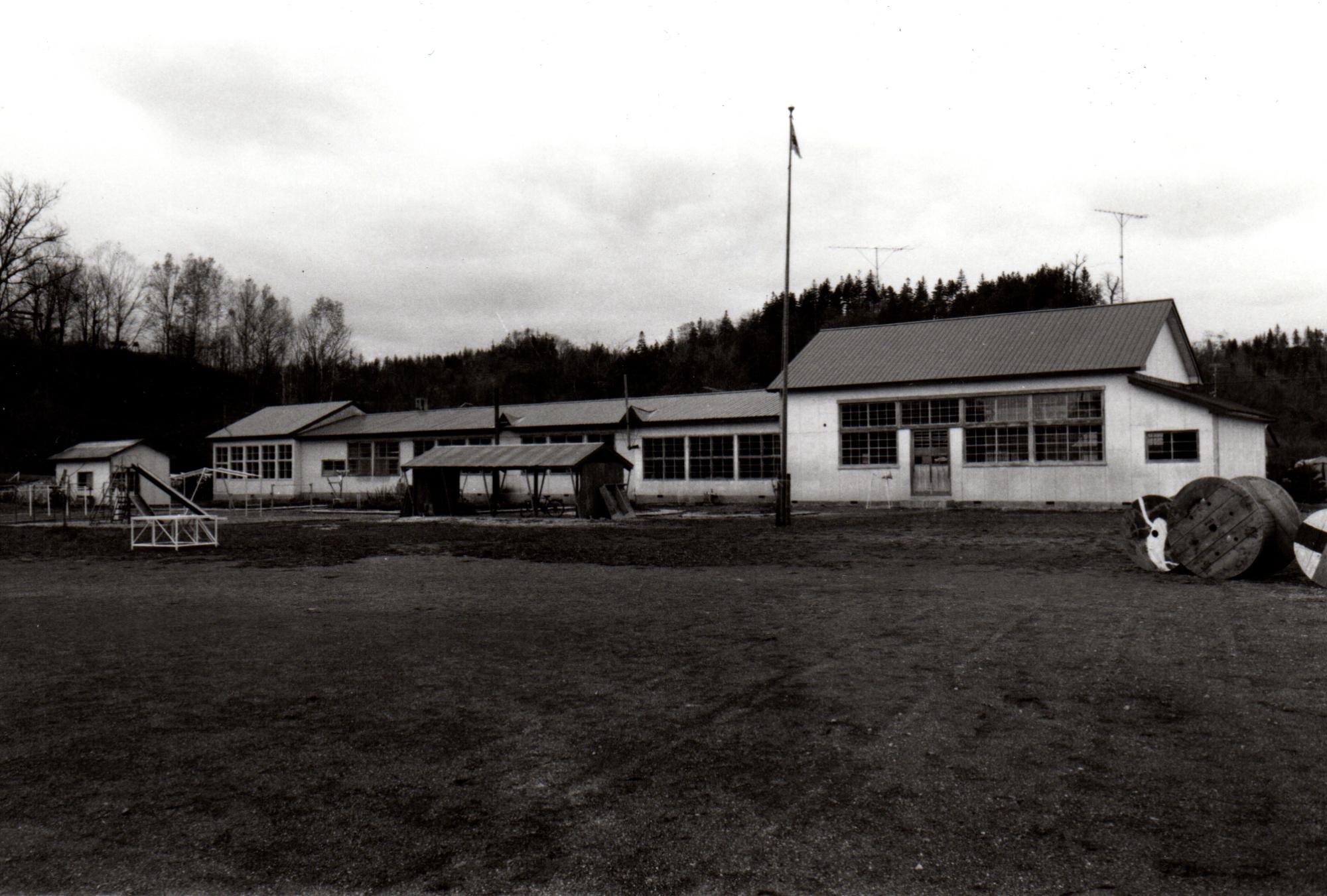 小高い丘の手前に建てられた校舎の前に駐輪場が設置されている旧三栄小学校校舎の白黒写真