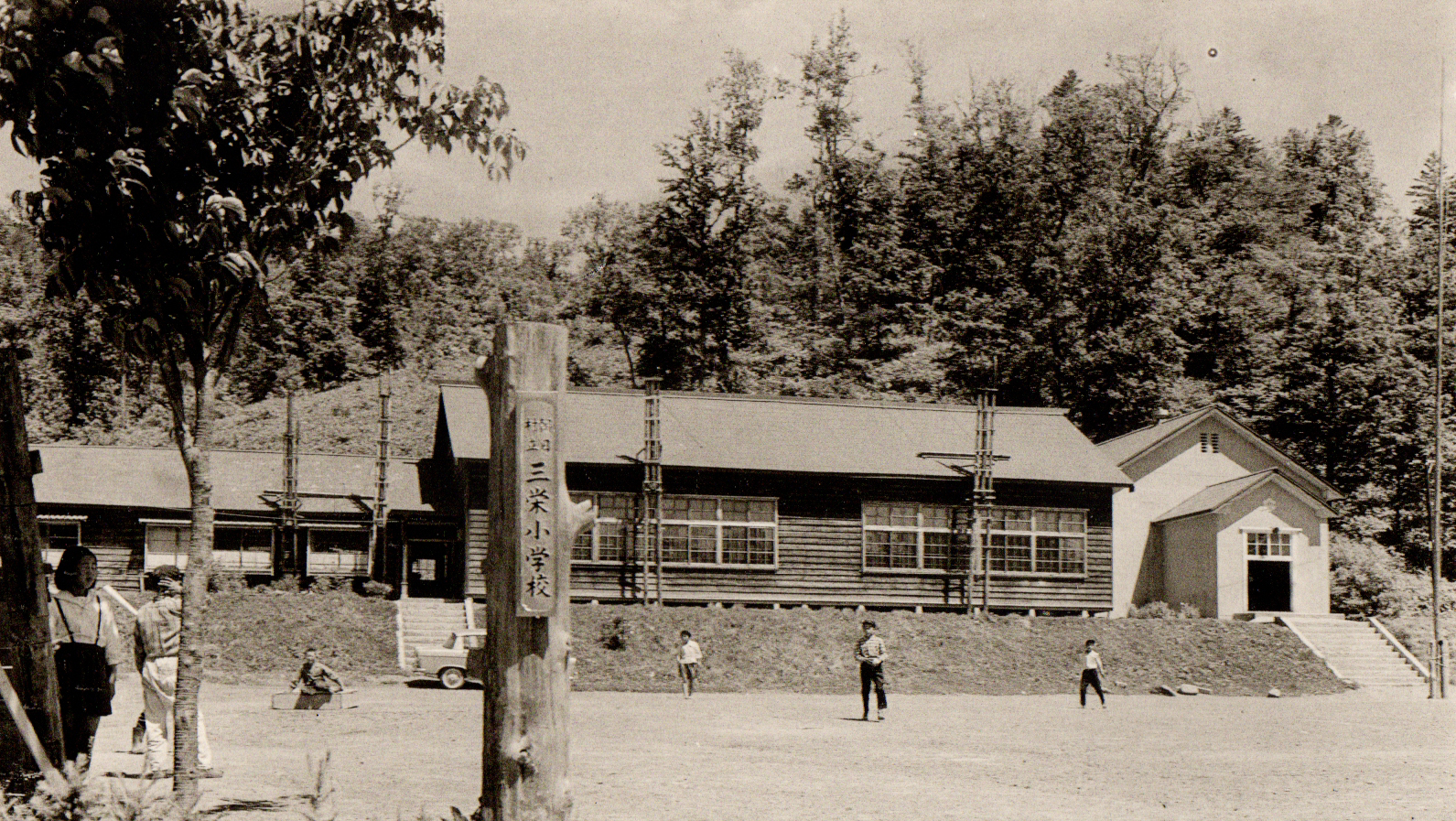 手前の運動場で児童が野球をしている奥の階段を上がった場所に建てられた昭和37年頃の旧三栄小学校校舎の白黒写真